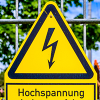 Gelbes Warnschild mit schwarzem Rand und einem schwarzen Blitz-Symbol in der Mitte